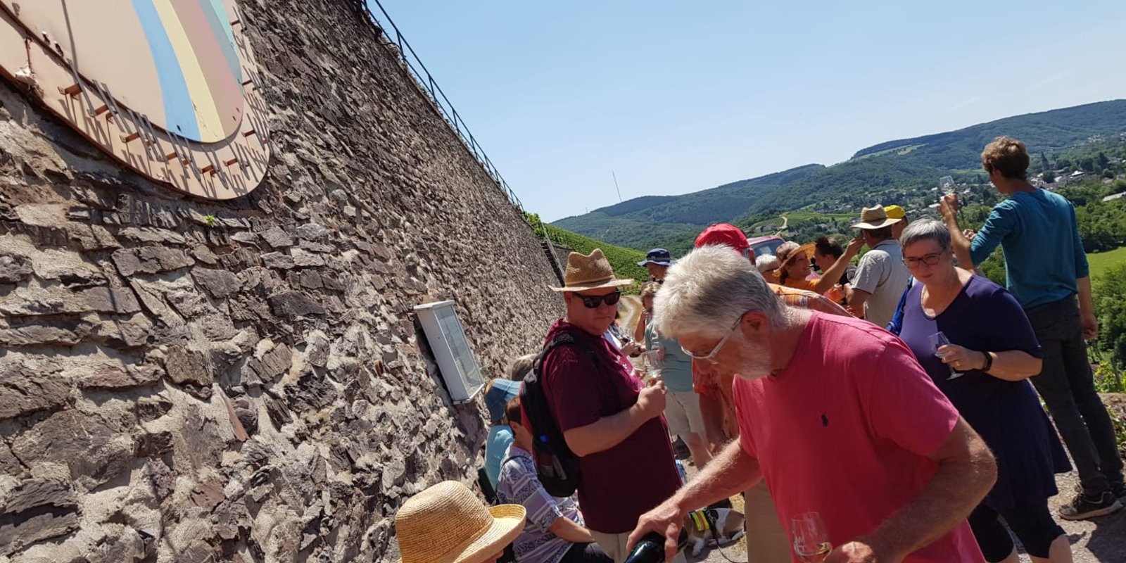 Bei strahlendem Sonnenschein schenkt ein Kultur- und Weinbotschafter Wein unterhalb einer Sonnenuhr aus. der Sonnenuhr 
